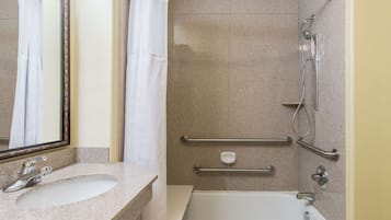 A bathroom with a sink, mirror, shower with grab bars, and a bathtub.