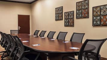 Un salón de conferencias con una larga mesa, sillas negras y decoración en la pared.