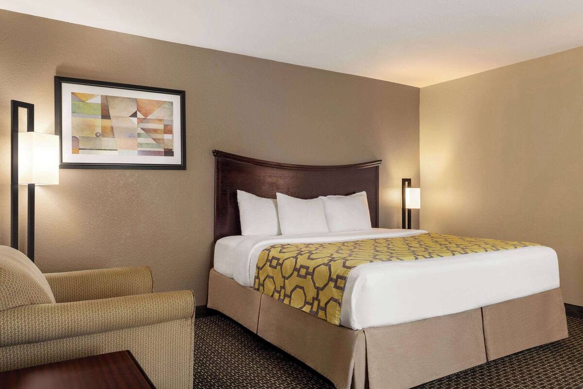 Una habitación de hotel con una cama, una silla y una obra de arte enmarcada en la pared.