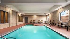 Una piscina con plataforma de baldosas, sillas y una puerta.