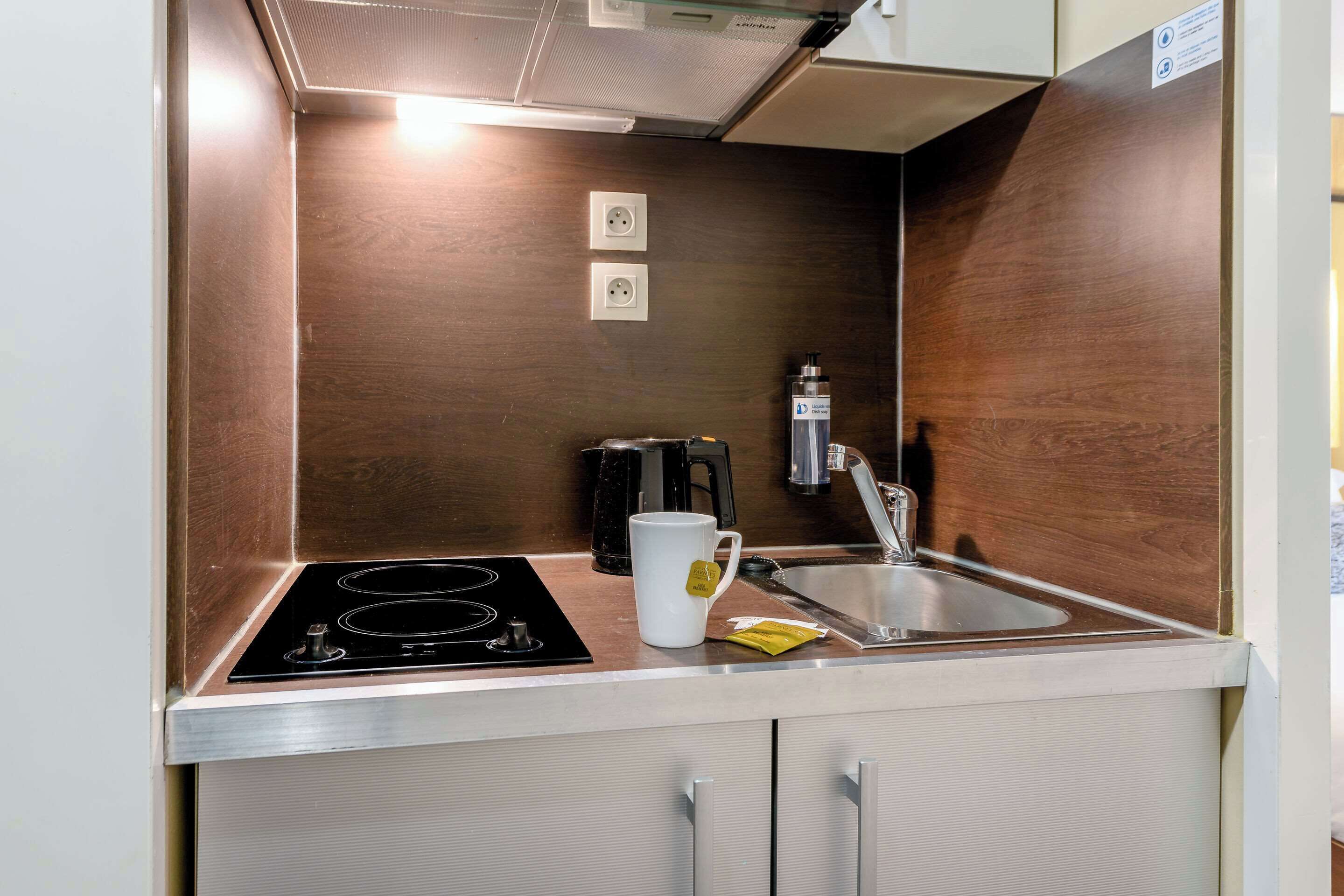 A compact kitchenette with a built-in stove, a sink, and two electrical outlets on the wall.