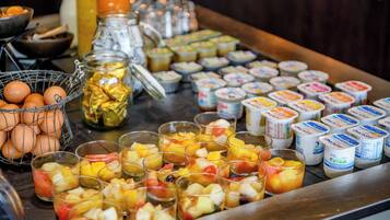 A breakfast buffet with various fruits, yogurt containers, and a basket of eggs.