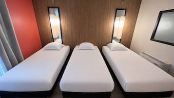 A hotel room with three single beds, a wooden accent wall, and a mounted TV.