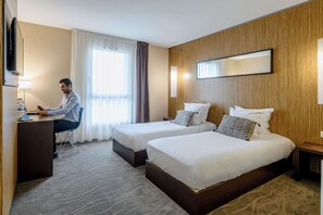 Una habitación de hotel con dos camas, un escritorio, un televisor y un ventanal con cortinas.