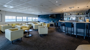 A modern lounge area with sofas and chairs, a bar with stools, and a large window offering a view.