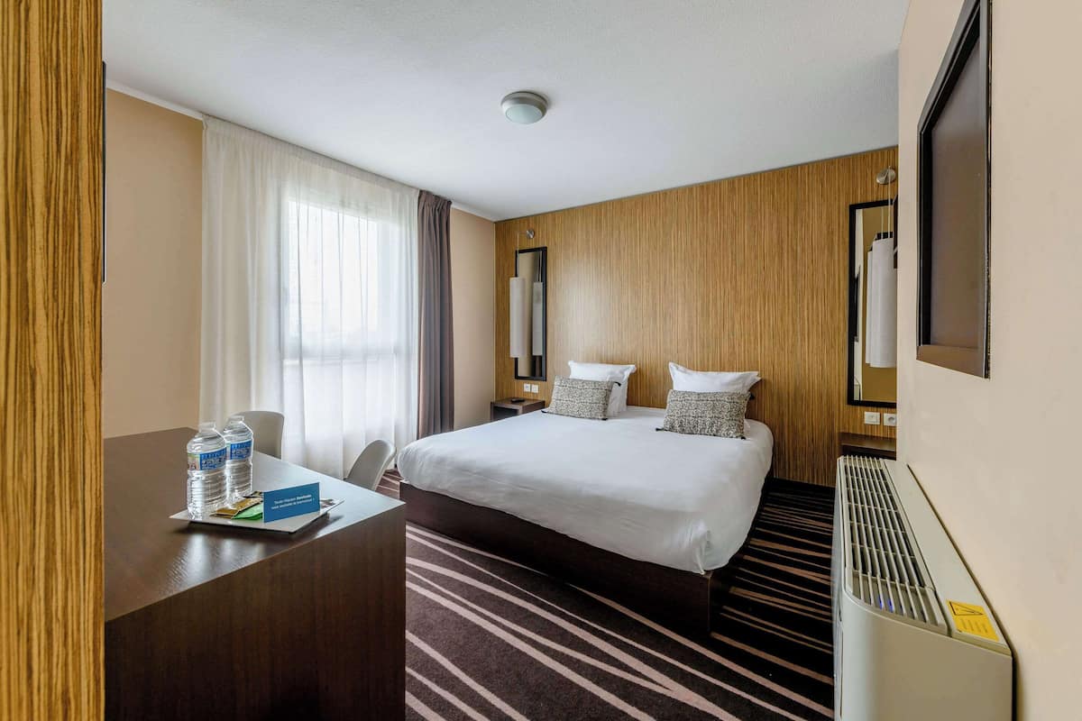 Une chambre d’hôtel avec un grand lit, un bureau avec une chaise, un distributeur d’eau et un thermostat.