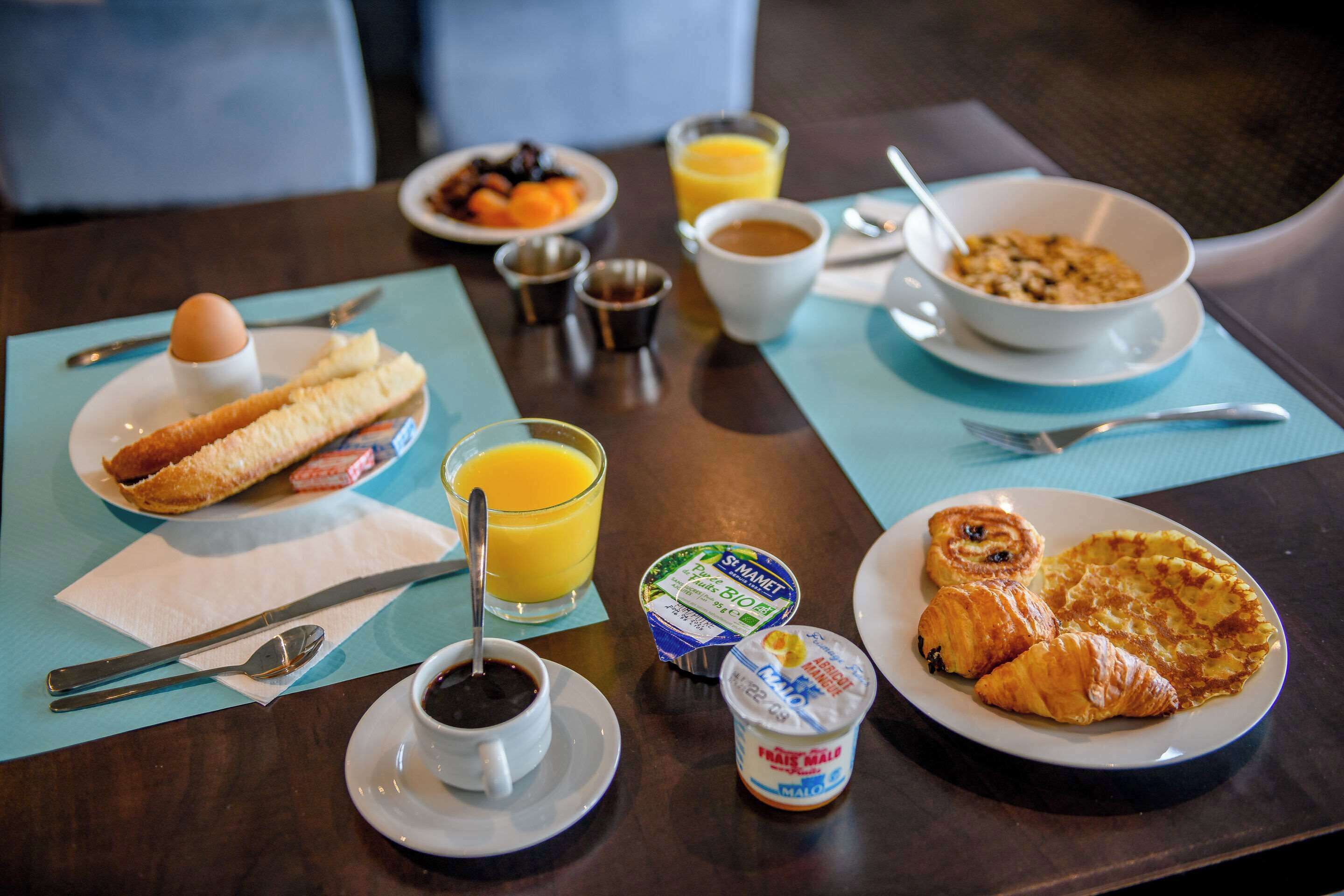 Ein Frühstückstisch mit Croissants, einer Schüssel Müsli, einem Glas Orangensaft, einer Tasse Kaffee und einem Teller Obst.
