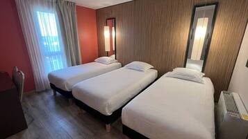 A hotel room with two beds, a desk, a chair, a heater, and a window with curtains.