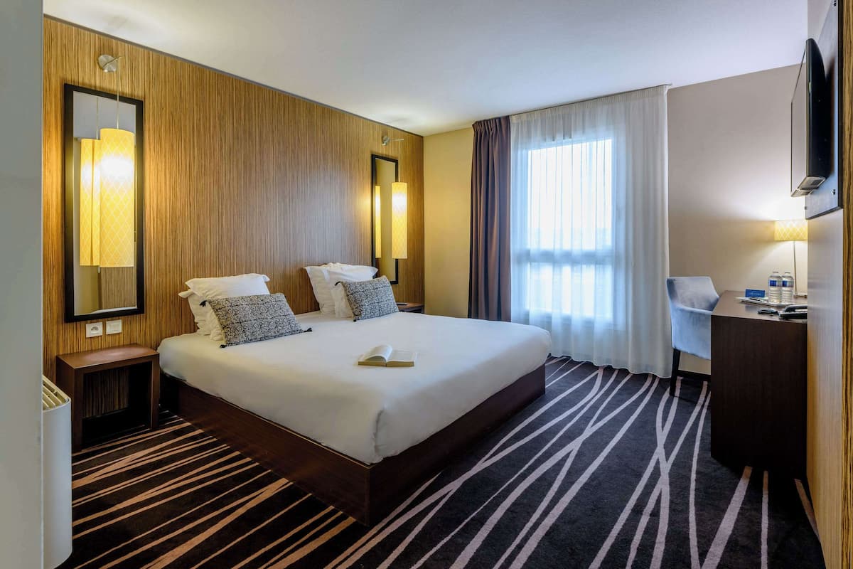 Une chambre d’hôtel avec un grand lit, un bureau, un miroir et une télévision.