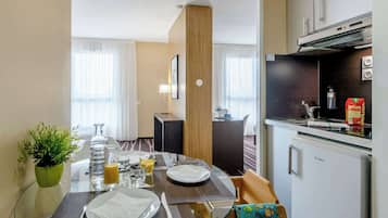 Ein Hotelzimmer mit Essbereich, ausgestattet mit einem Glastisch, Stühlen und einem kleinen Kühlschrank.