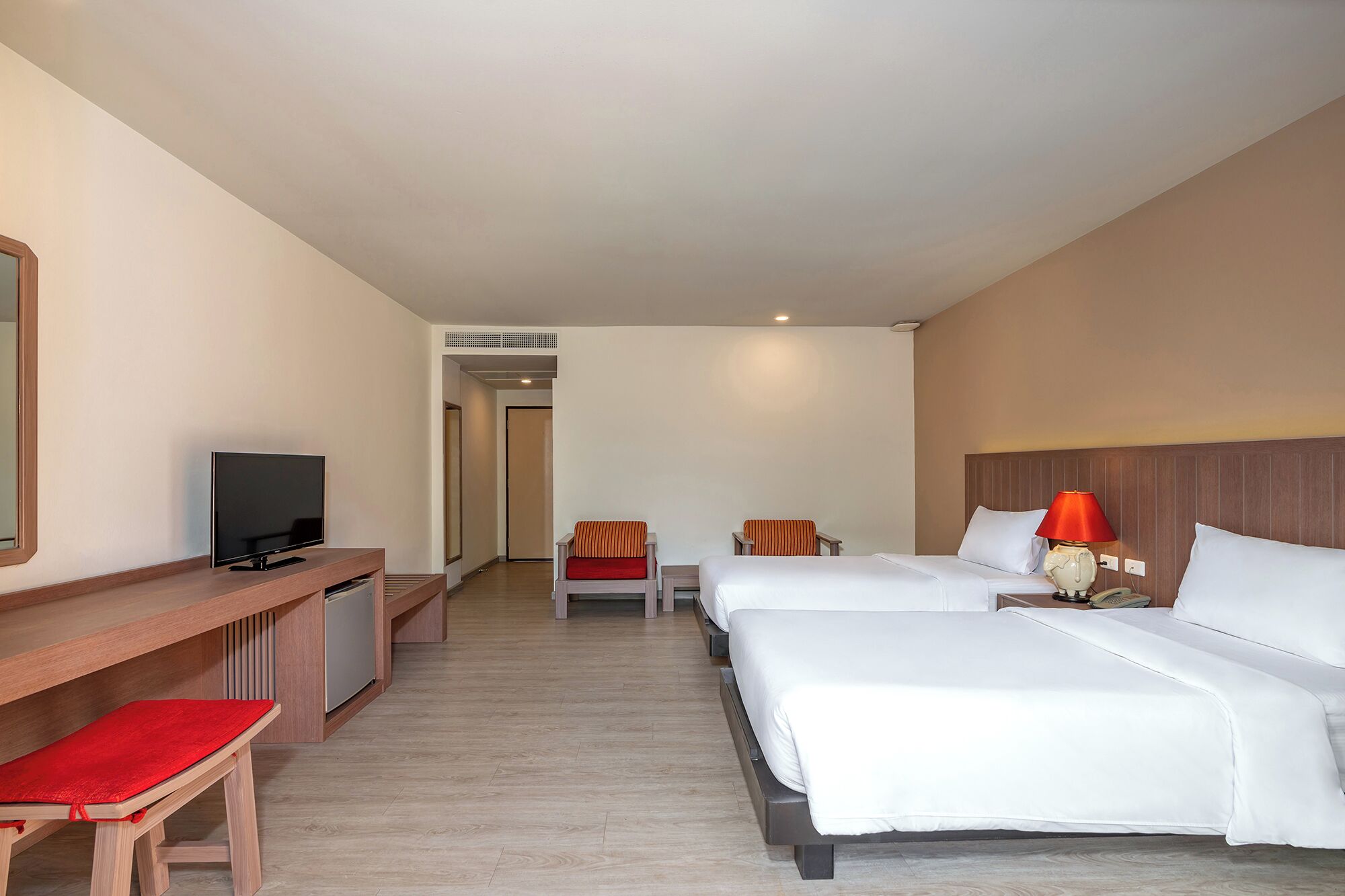 A hotel room with two beds, a desk with a TV, a chair, and a lamp.