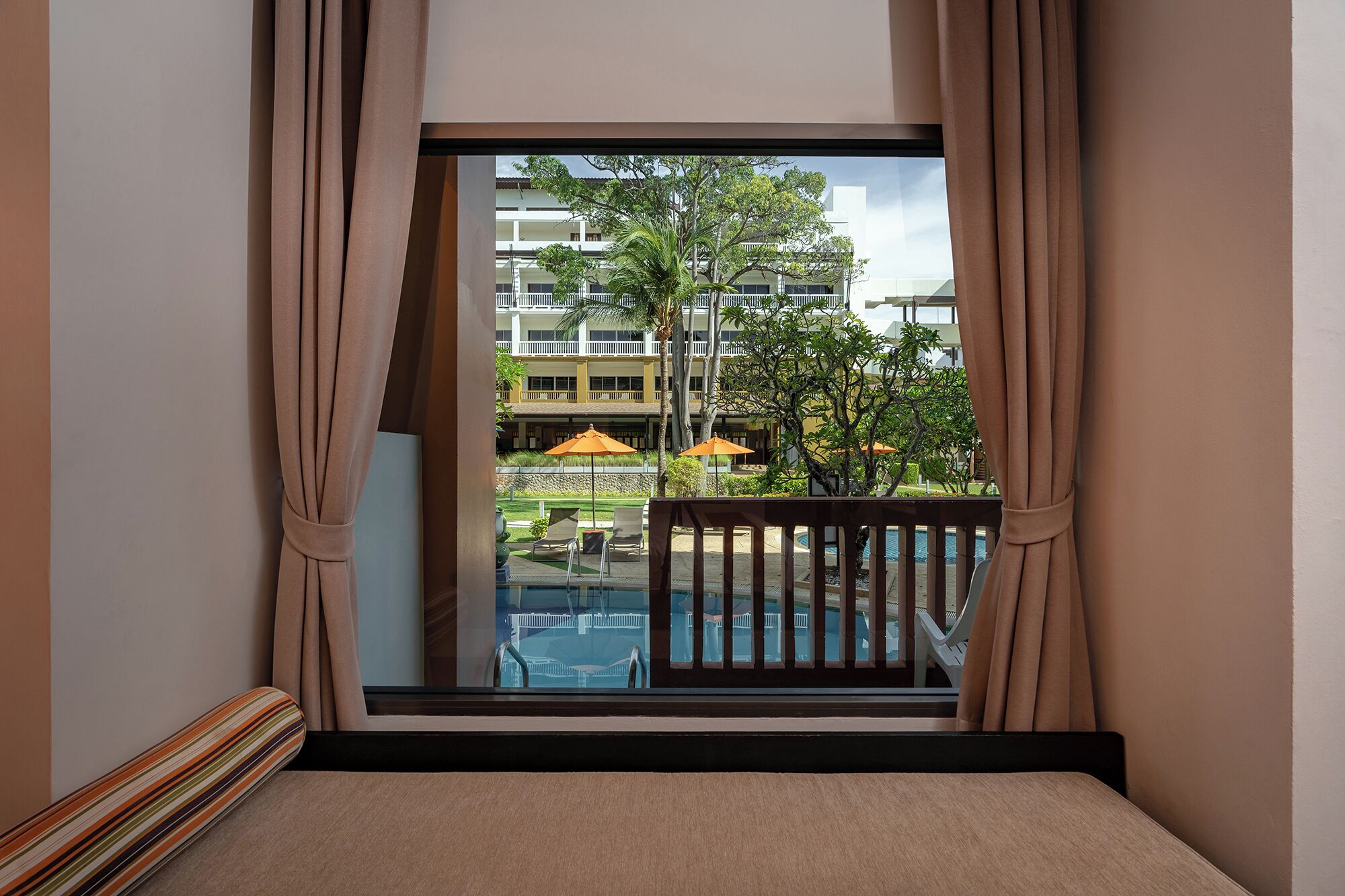A hotel room with a large window, a balcony with a pool, and outdoor umbrellas.