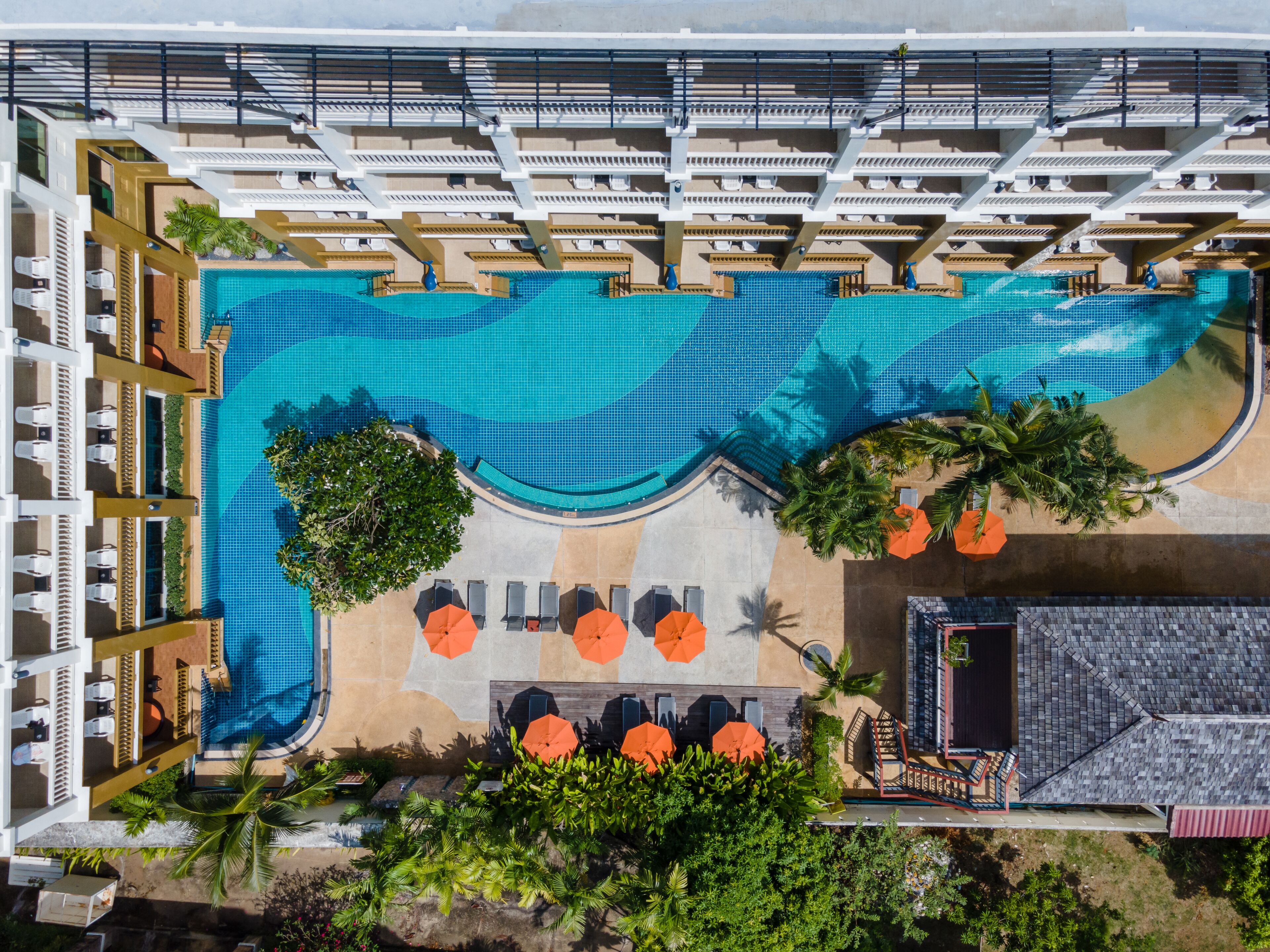 A large pool with multiple levels of seating and sun loungers, surrounded by palm trees and shaded areas.