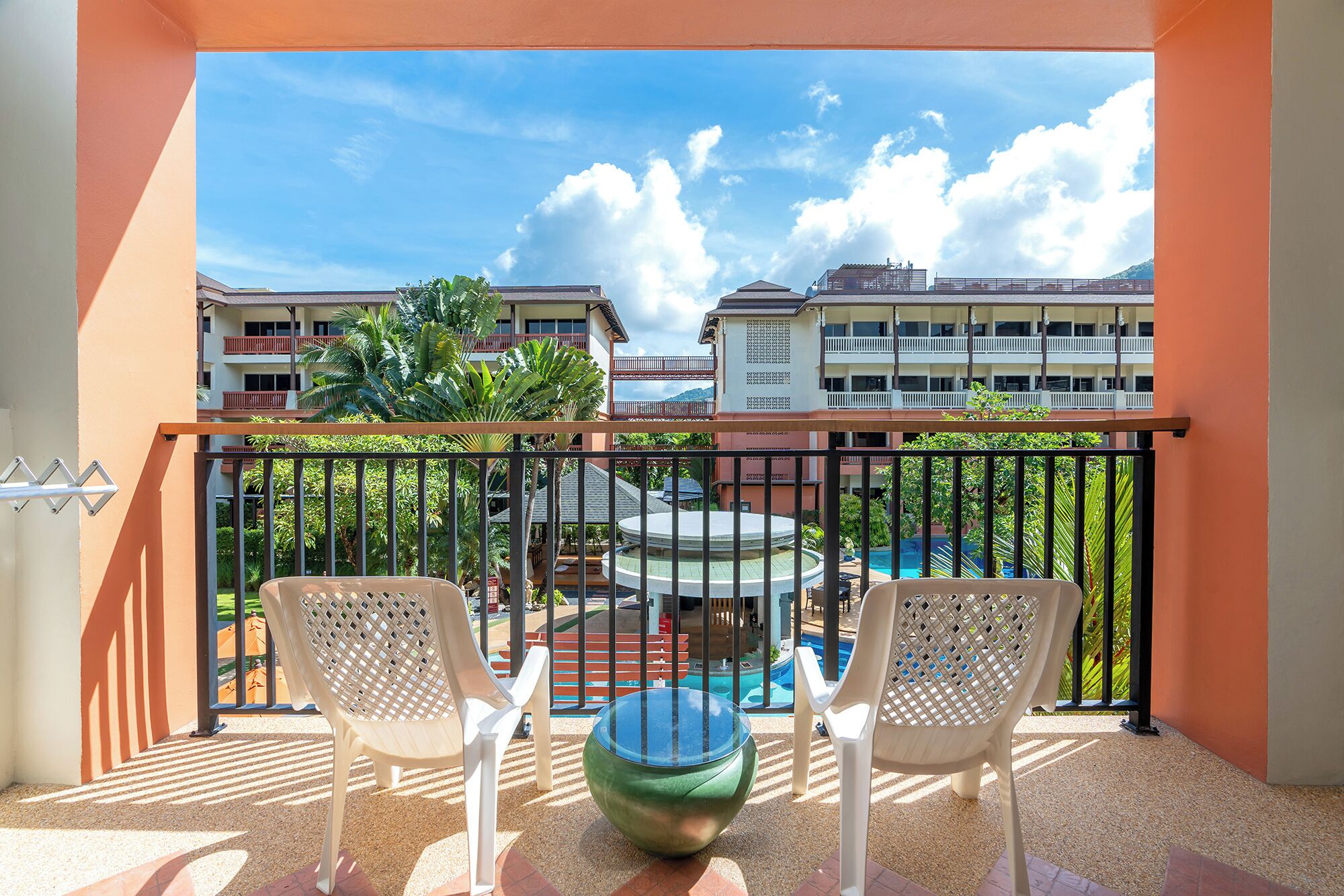 A balcony with two white plastic chairs and a green bowl, overlooking a pool and buildings.