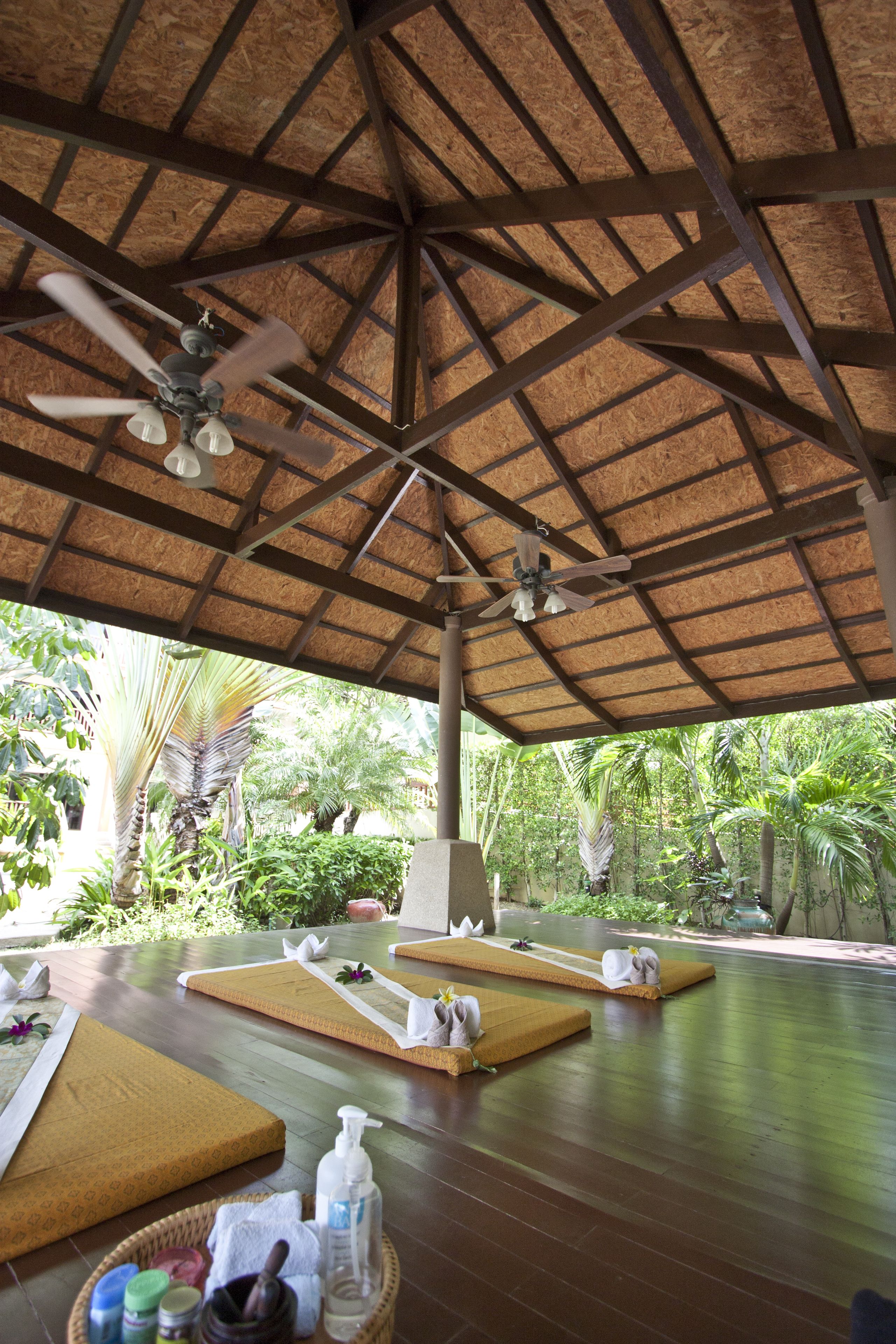 A spa area with wooden floors, thatched roof, and multiple massage tables.