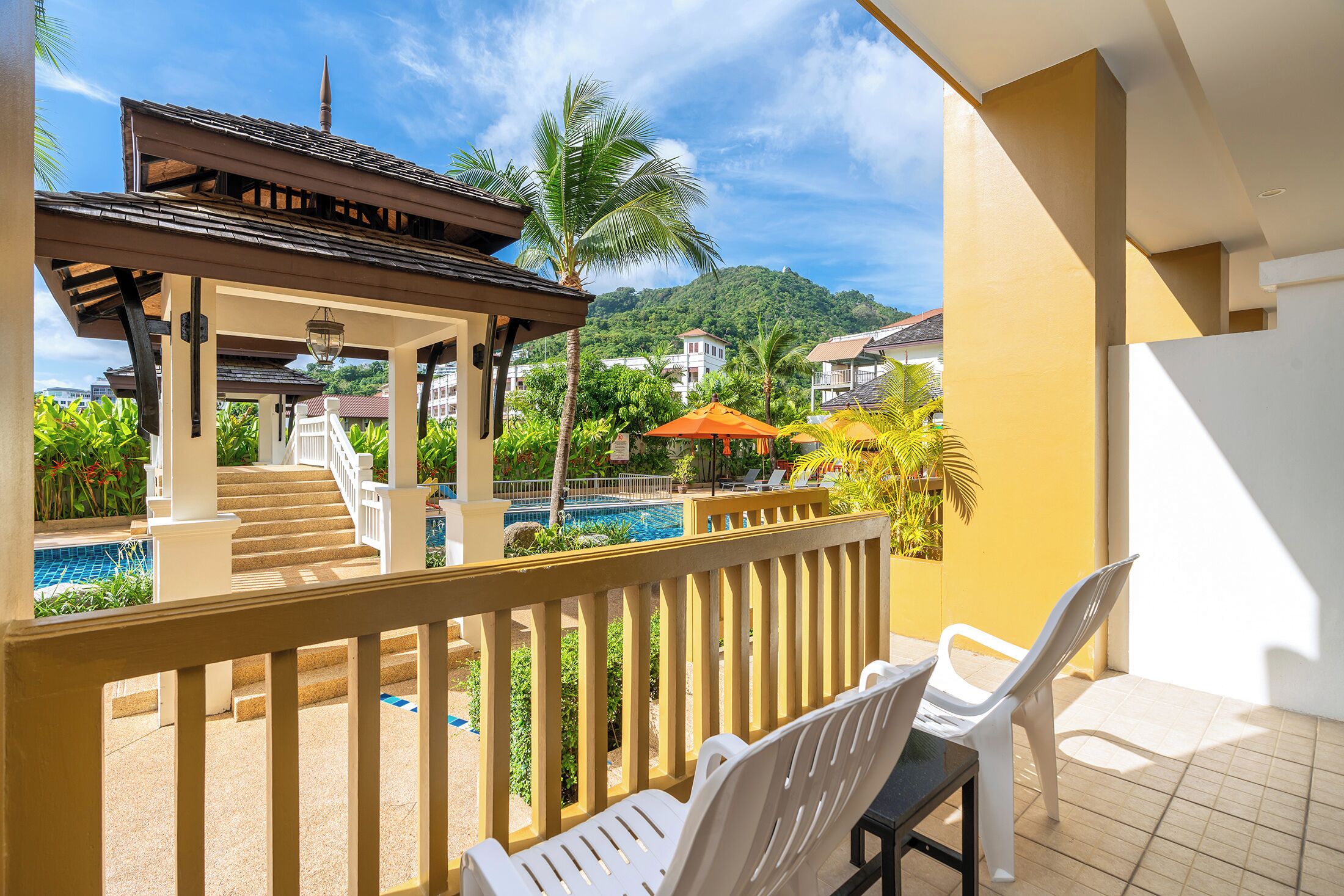 A balcony with a pool, white chairs, and a covered area with stairs leading to a pool.