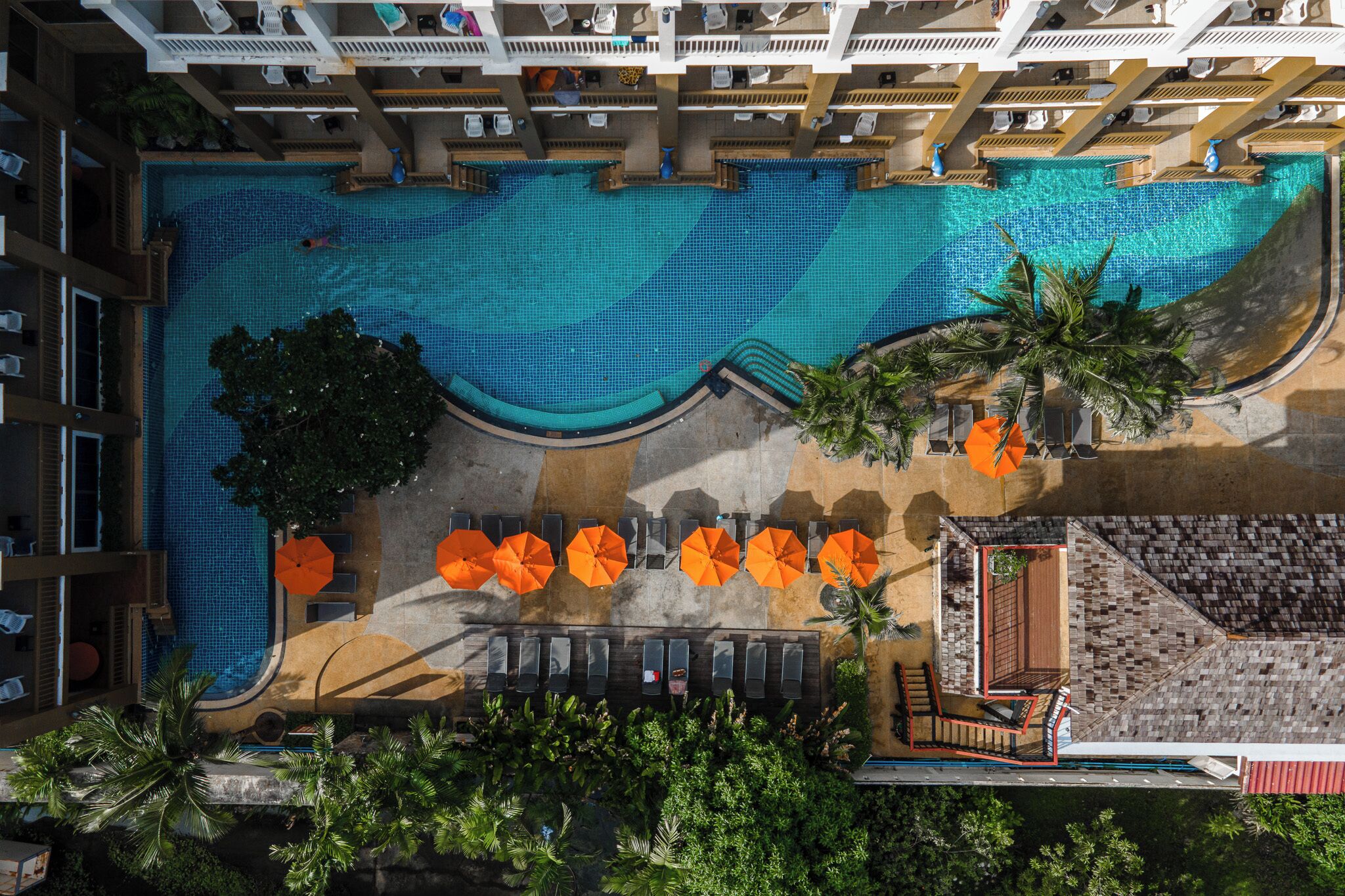 Vista aérea de un hotel con una gran piscina, tumbonas y sombrillas.