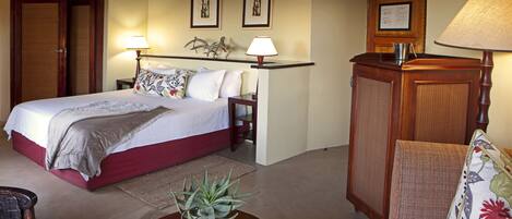 A bedroom with a bed, bedside lamps, a nightstand, a chair, a table with a plant, and a door.