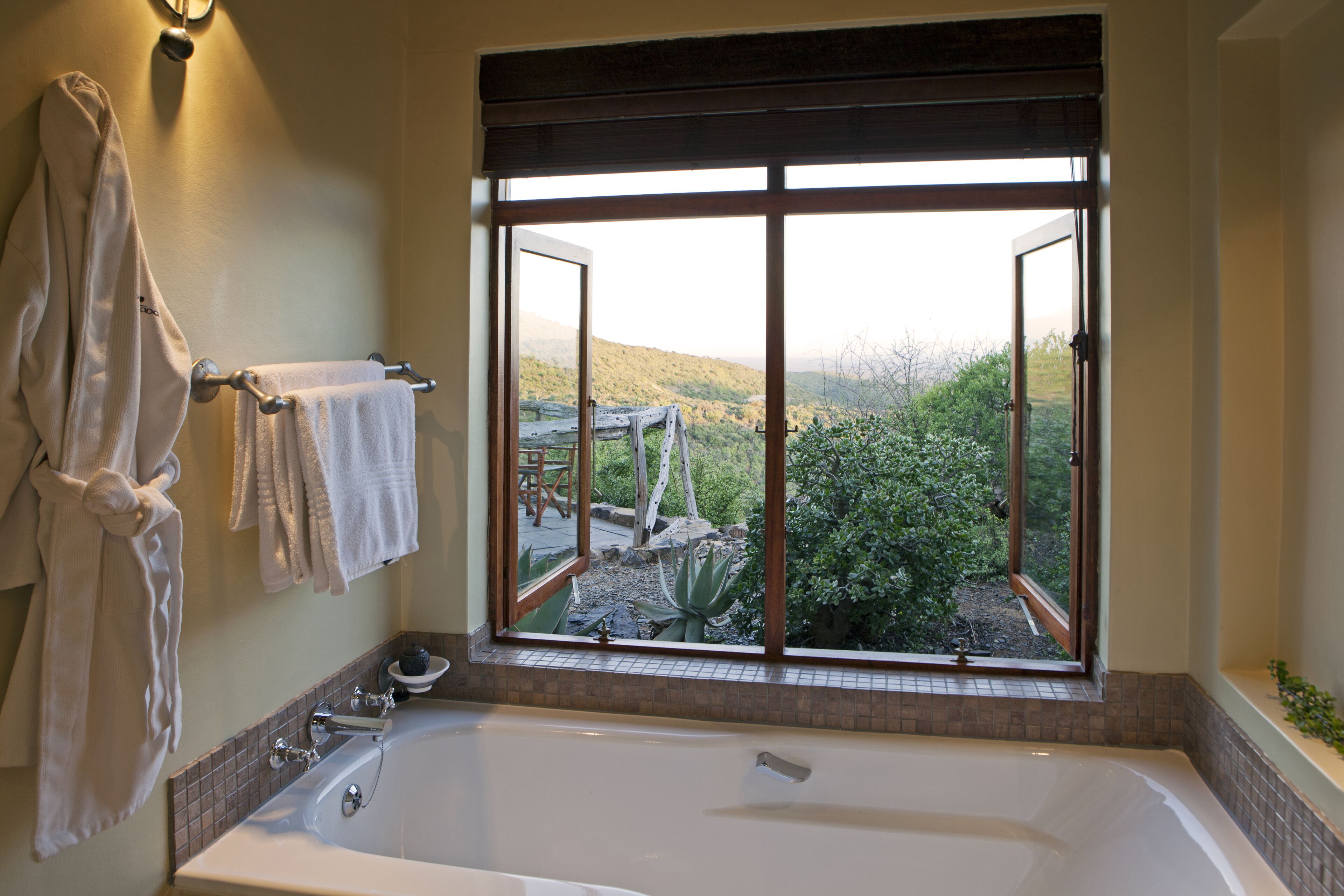 Ein Badezimmer mit einer großen Badewanne, einem Fenster mit Gartenblick und Handtüchern auf einem Wäscheständer.