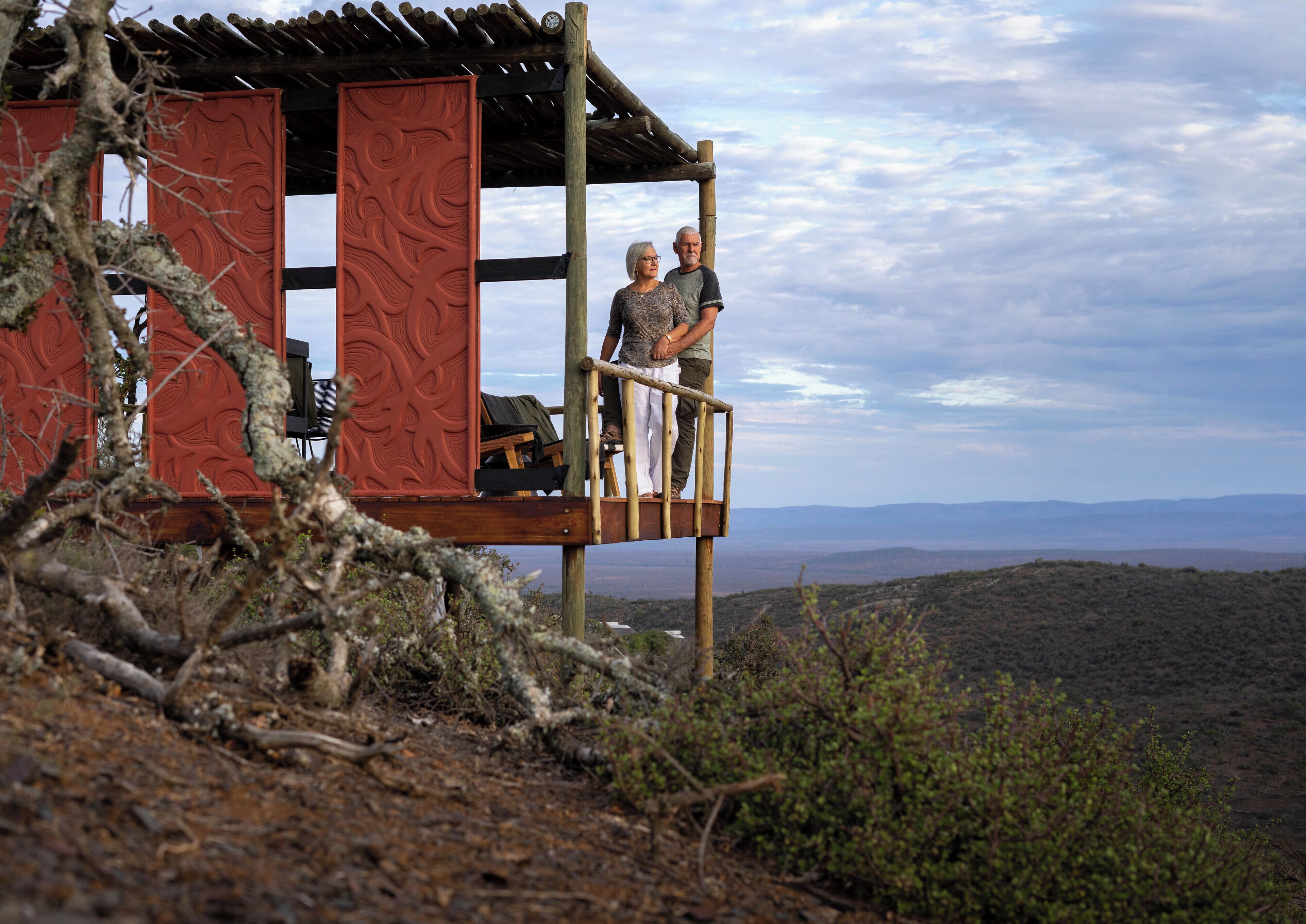 Una cabaña de madera con fachada roja y un balcón con vistas a un paisaje montañoso.