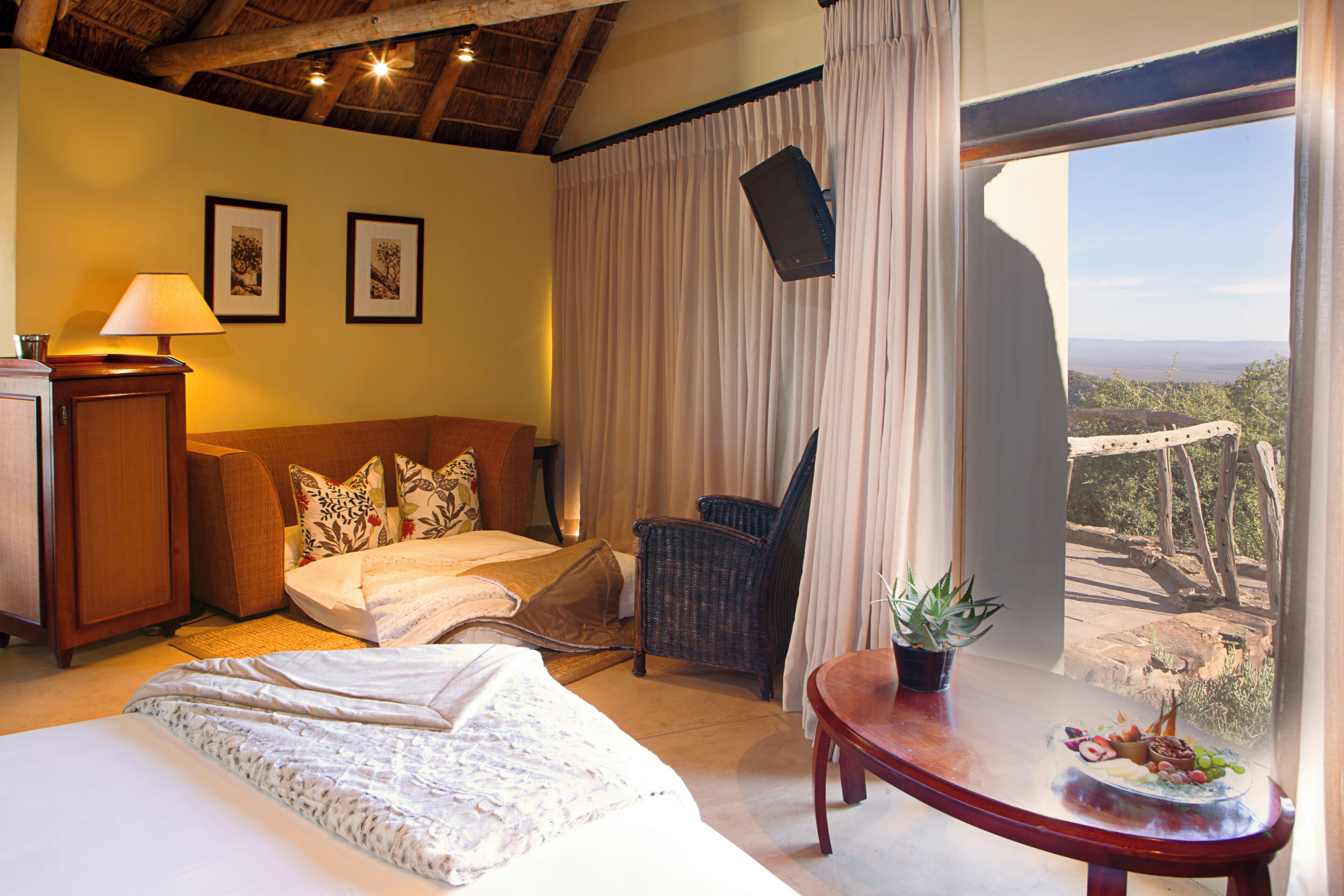 A hotel room with a bed, a chair, a table with a plant, and a view of the outdoors.