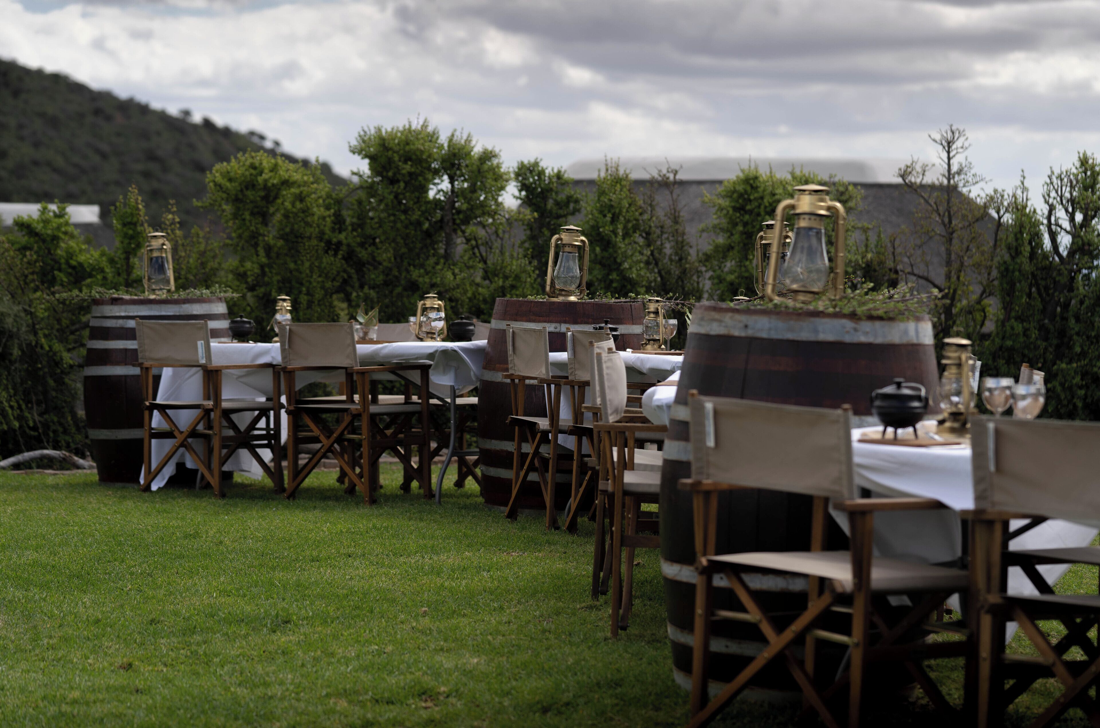 Zona de comedor al aire libre con mesas y sillas, rodeada de vegetación y montañas al fondo.