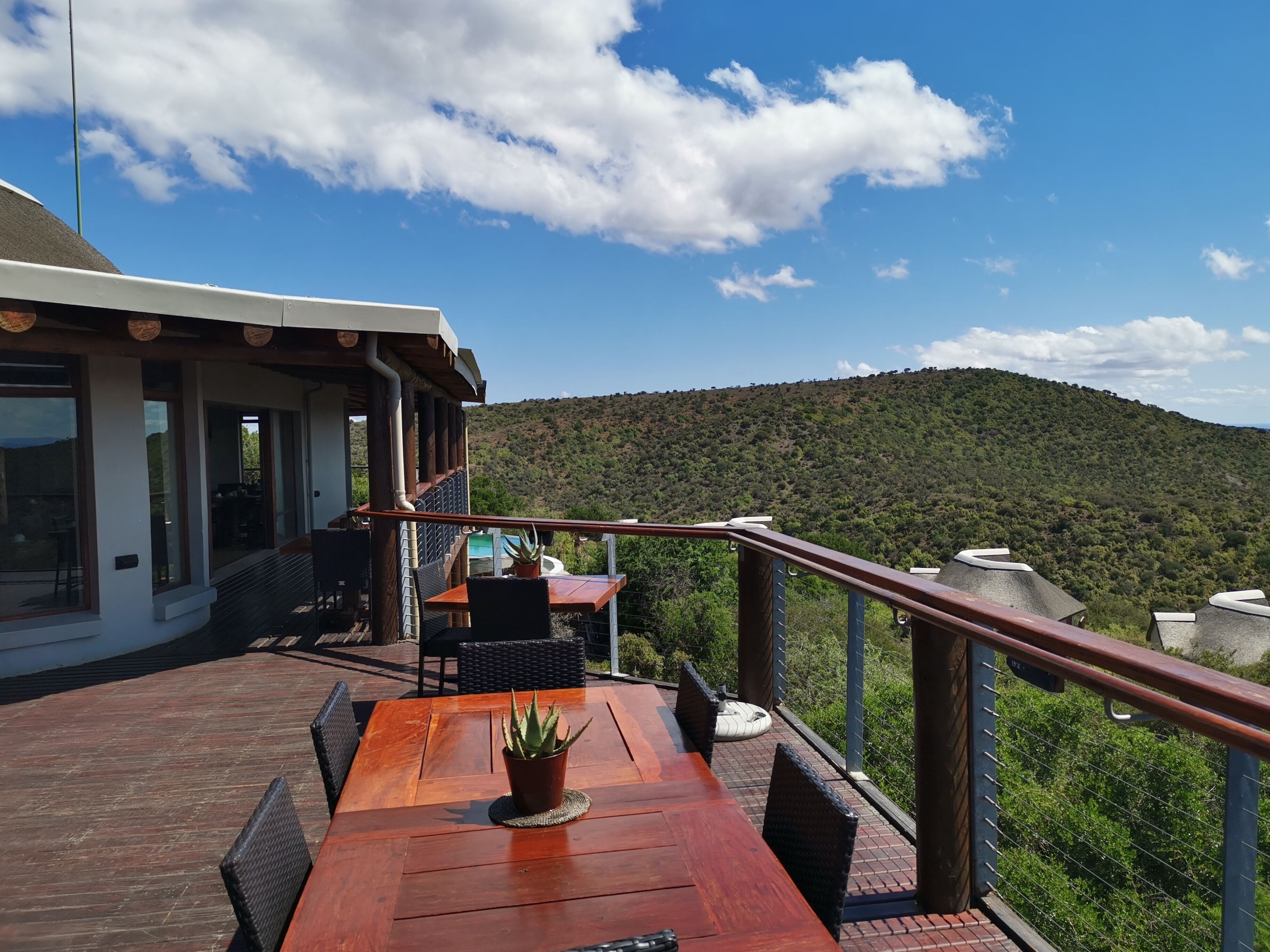 A wooden deck with a table and chairs, a potted plant, and a view of a hilly landscape.