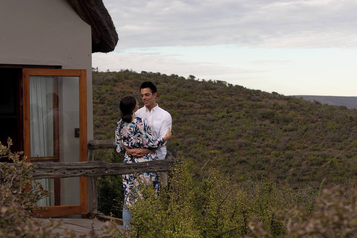 A couple embracing on a balcony with a view of a hilly landscape.