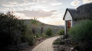 A pathway leading to a house with a thatched roof, surrounded by greenery and hills. - Kuzuko Lodge (Blue Crane Route)