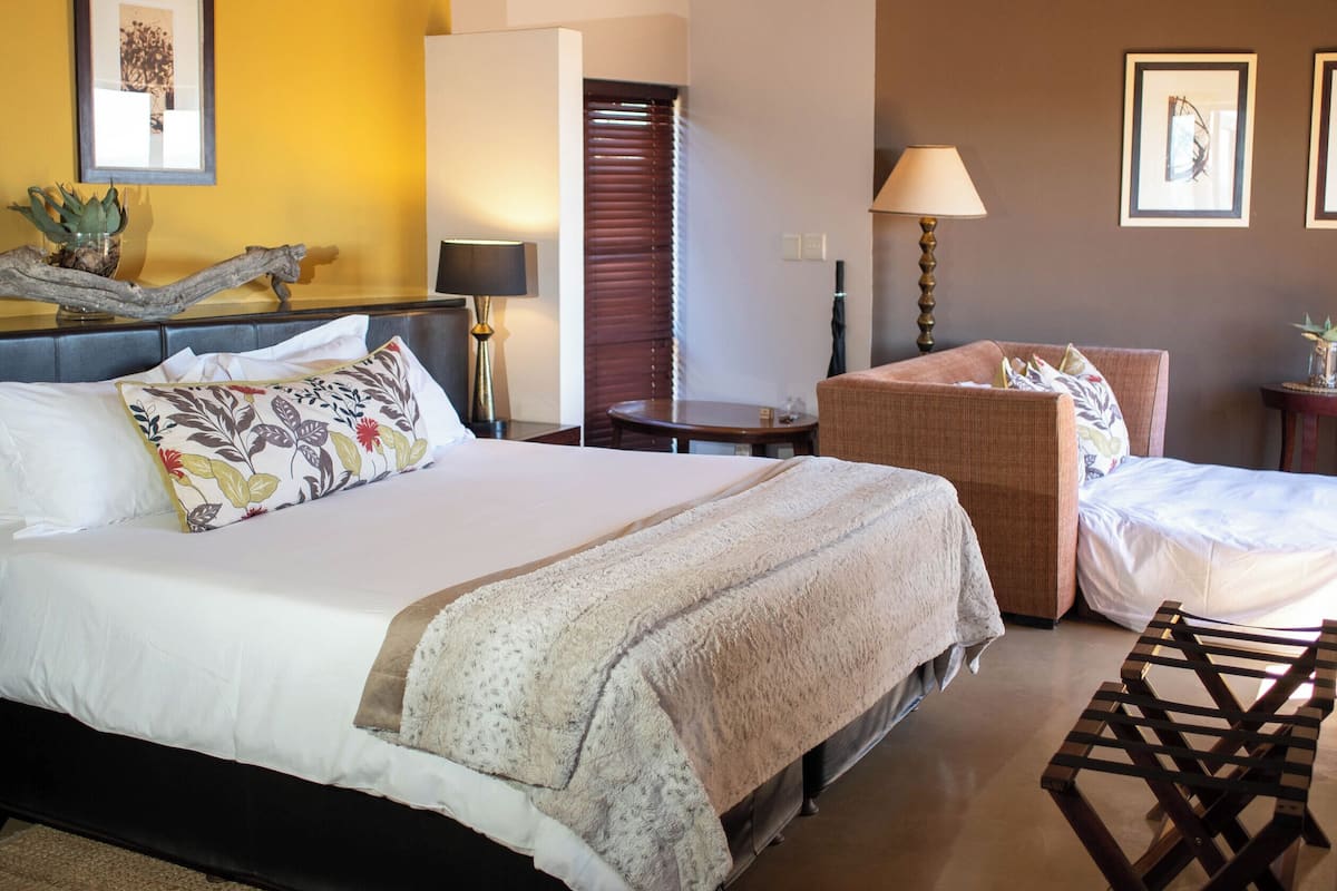 A room with a bed, a chair, a lamp, and a wooden ceiling.