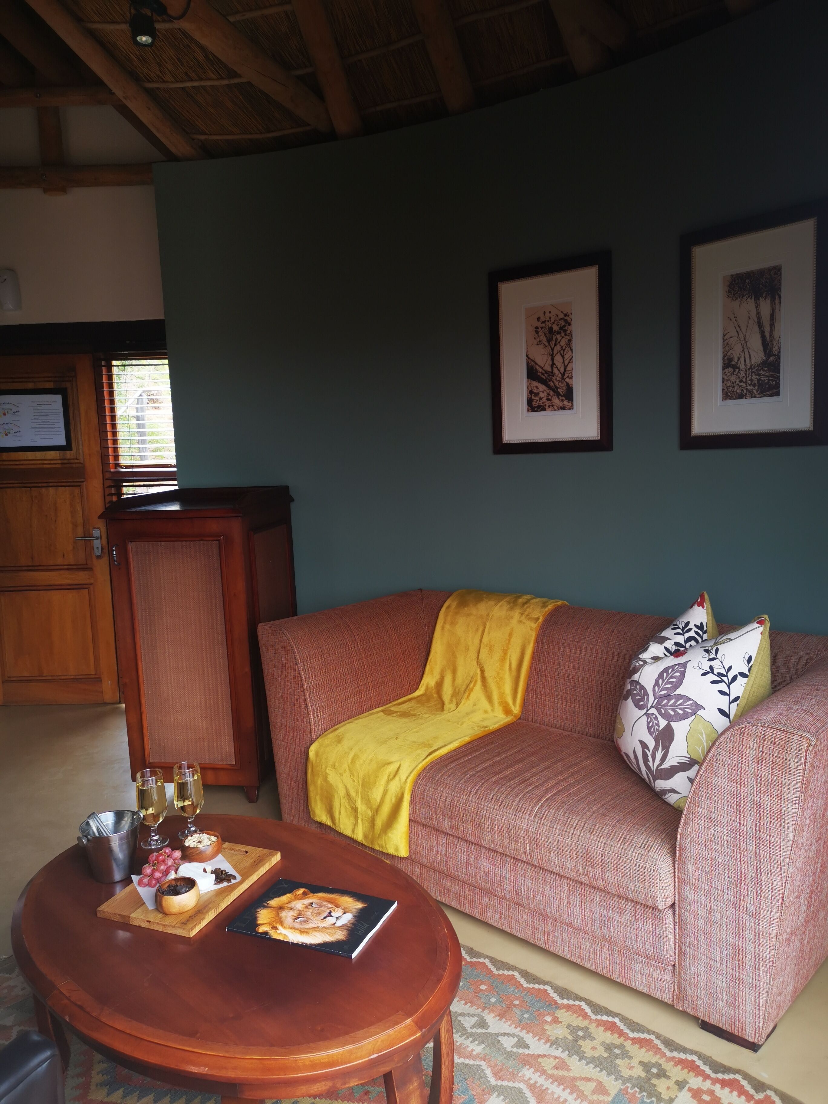 Una sala de estar acogedora con techo de madera, un sofá rojo con una manta amarilla, una mesa de centro de madera con un libro y aperitivos, y cuadros en la pared.