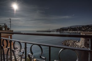 Un balcon offrant une vue sur une mer calme, un quai situé au loin et une côte rocheuse.