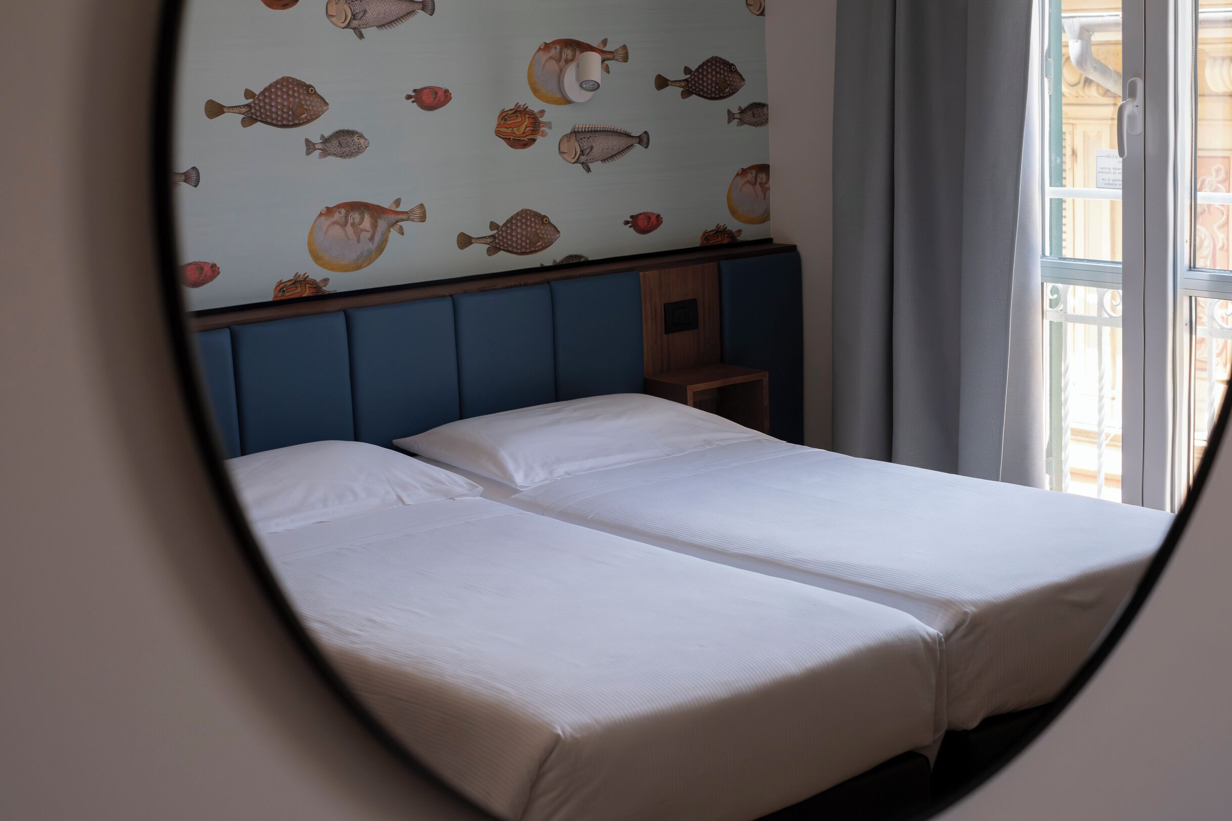 A room with two beds, a blue headboard, and a wall with fish patterns.
