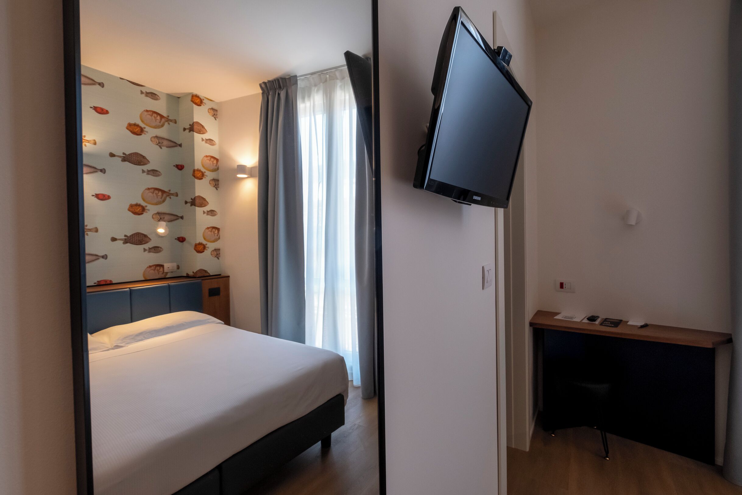 Une chambre d’hôtel équipée d’un lit, d’un bureau, d’un téléviseur à écran plat et d’une fenêtre avec des rideaux.