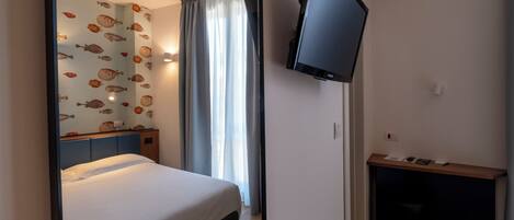 A hotel room with a bed, a desk, a flat-screen TV, and a window with curtains.