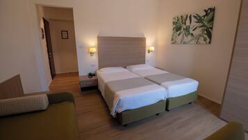 Habitación de hotel con dos camas, un sofá, una mesita de noche y una lámpara de pared.