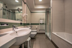 Un baño moderno con dos lavamanos, inodoro, ducha con mampara de vidrio y bañera.