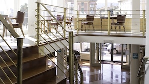 Un interior amplio con una escalera que lleva a un balcón, un comedor con sillas y ventanas grandes con vistas a la ciudad.