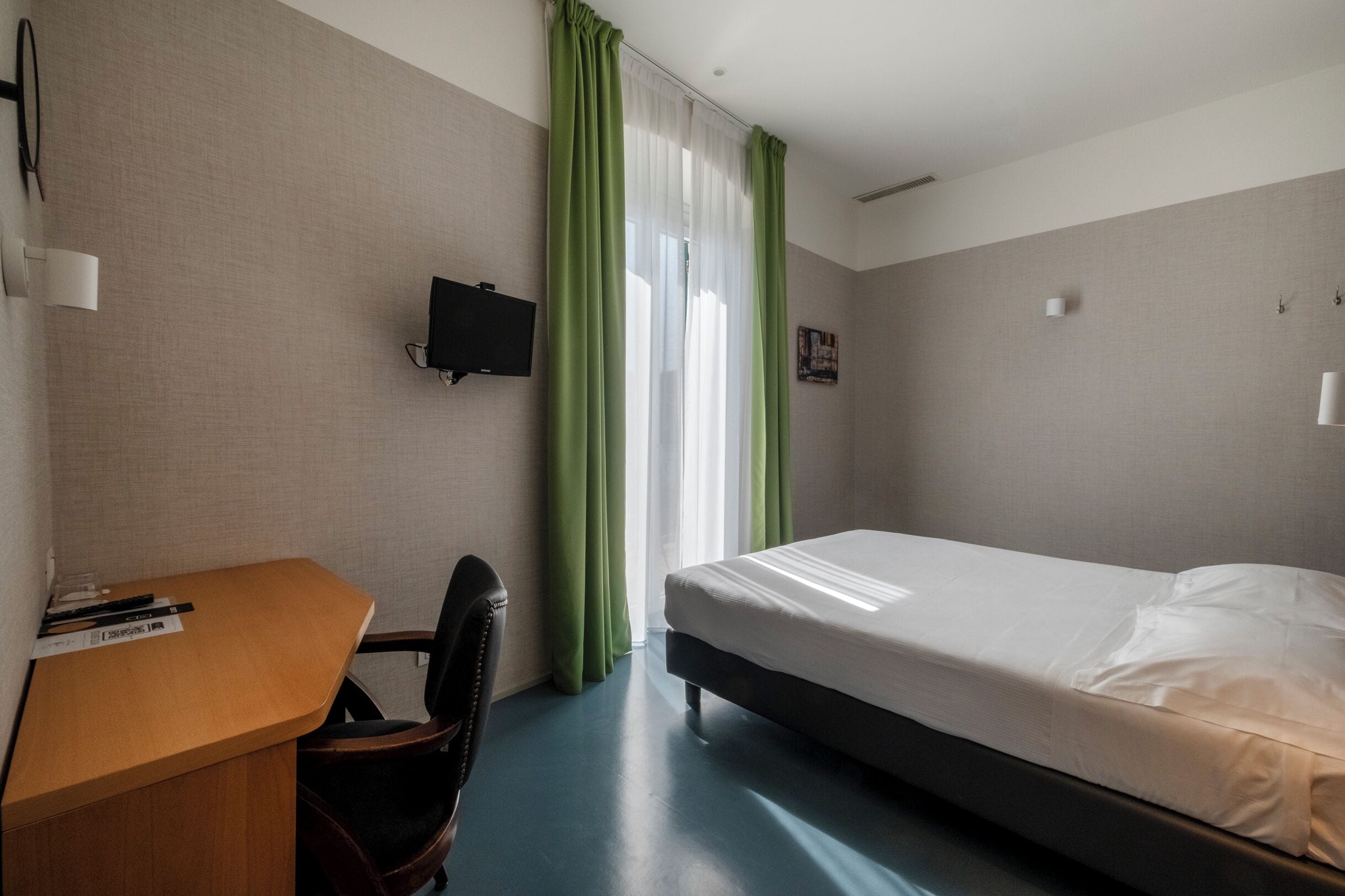 A hotel room with a bed, a desk, a chair, a television, and a window with curtains.