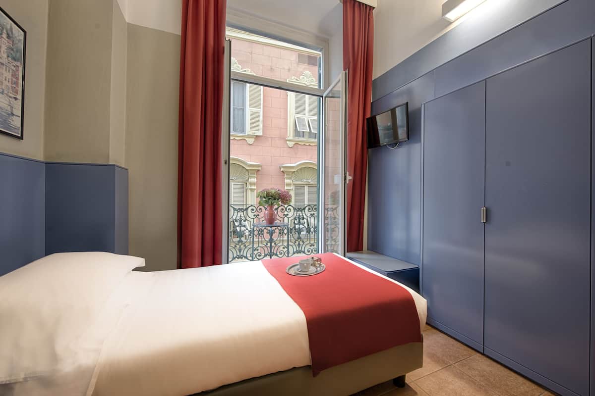 Une chambre d’hôtel avec un lit, une armoire, une télévision et une fenêtre avec des rideaux rouges.