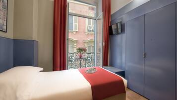 Una camera d'albergo con un letto, un armadio, una TV e una finestra con tende rosse.