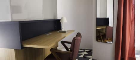 A modern room with a wooden desk, a chair, a lamp, a mirror, and a geometric patterned floor.