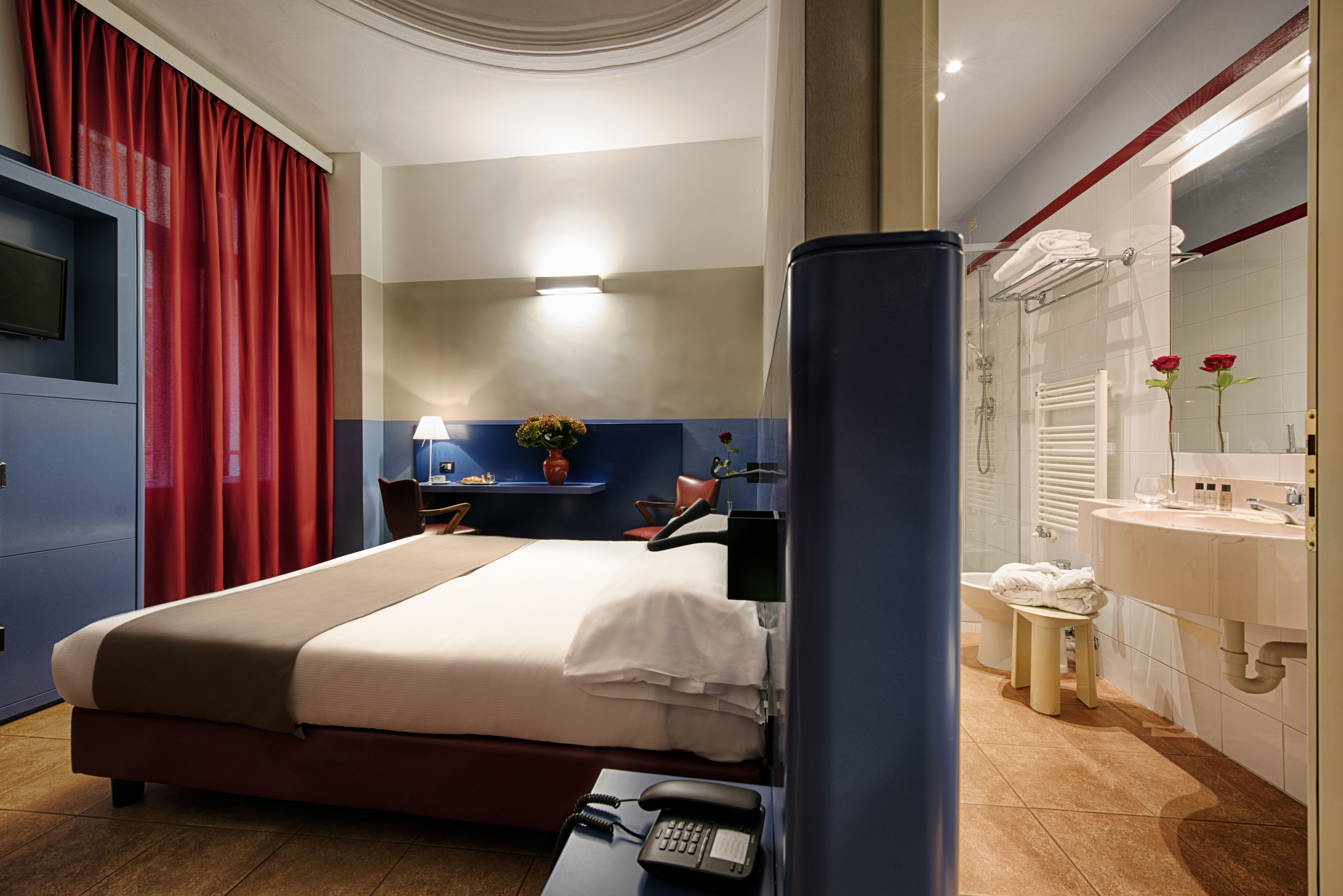 A hotel room with a bed, bedside table, lamp, and a bathroom with a sink and mirror.