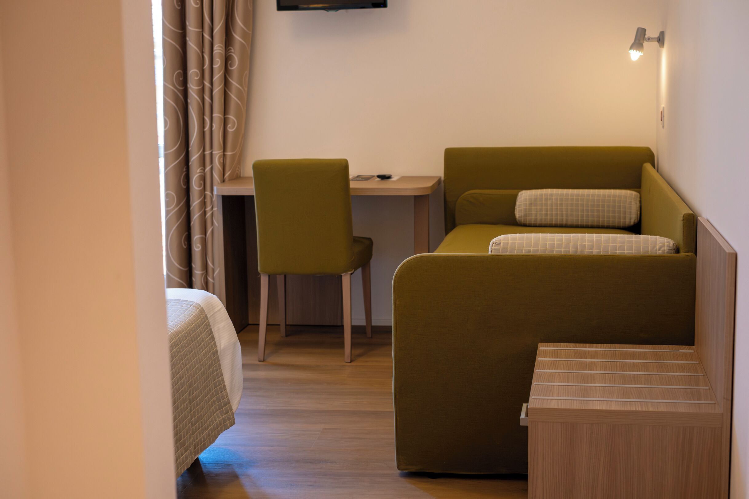 Een kleine kamer met een bed, een bureau, een stoel en een tafeltje.