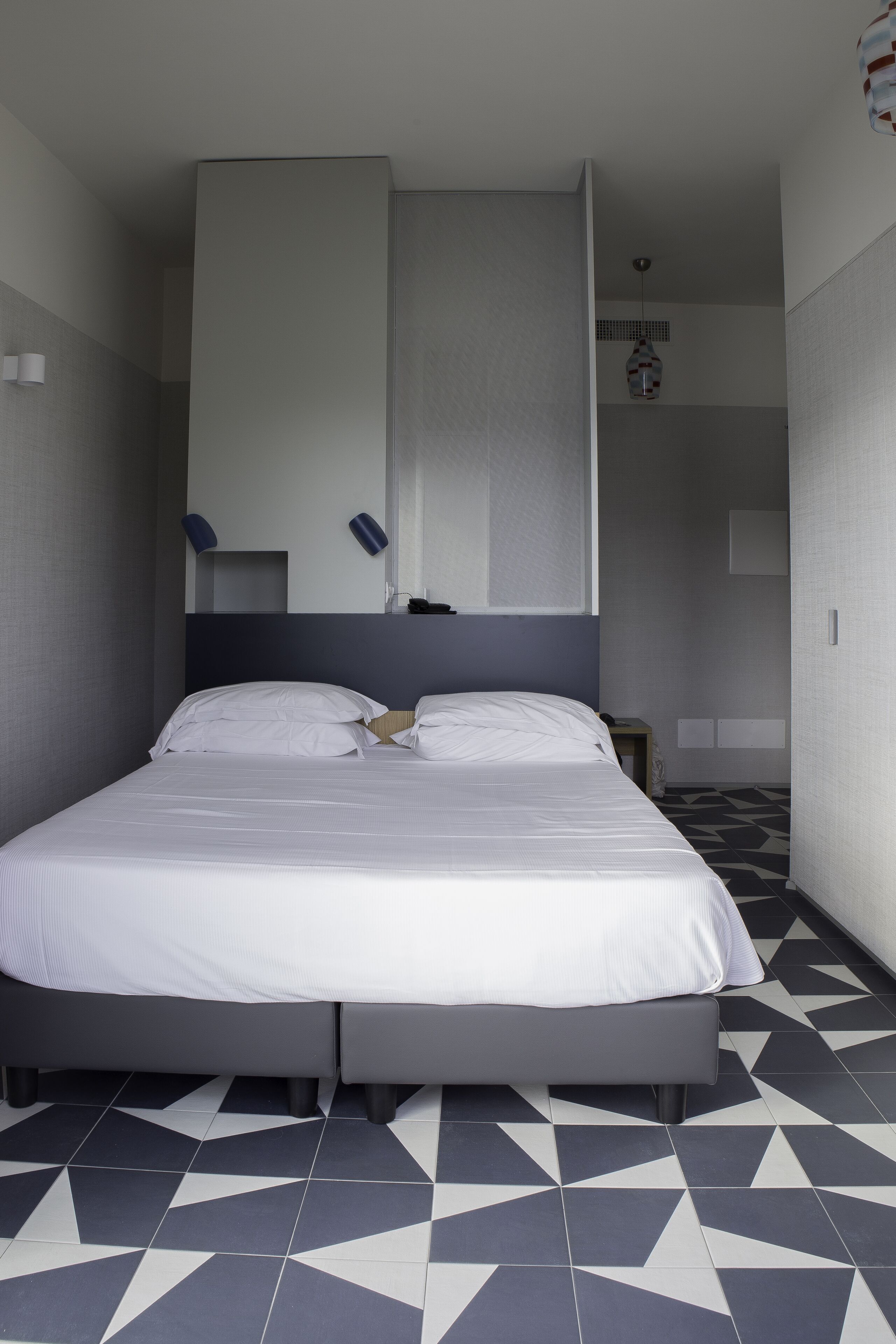 A modern hotel room with a large bed, a built-in wardrobe, and a geometric patterned floor.