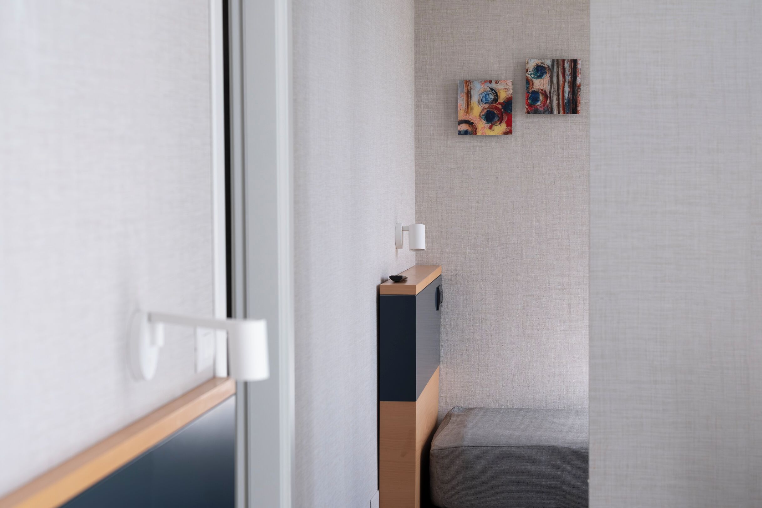 Habitació minimalista amb un llit, una taula de nit i dos quadres abstractes a la paret.