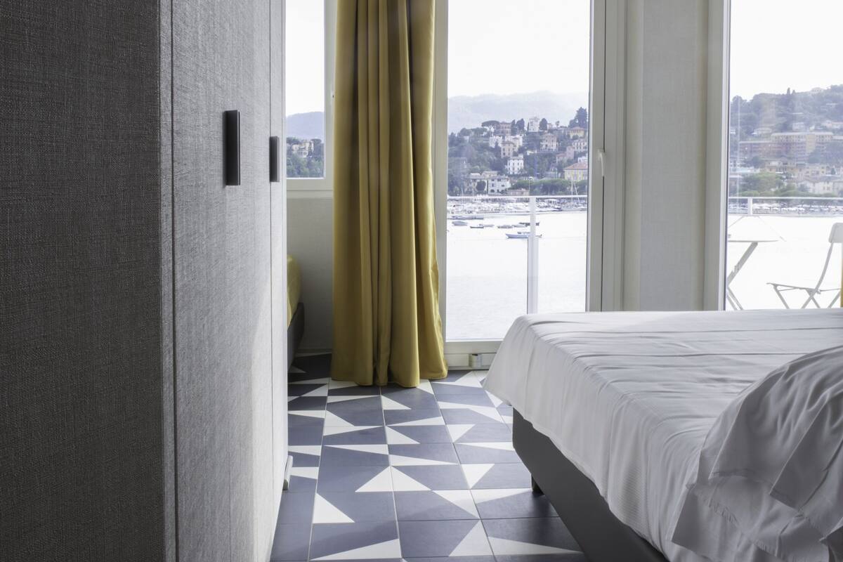 Une chambre d’hôtel avec un lit, une vue sur la ville et un sol orné de motifs géométriques.