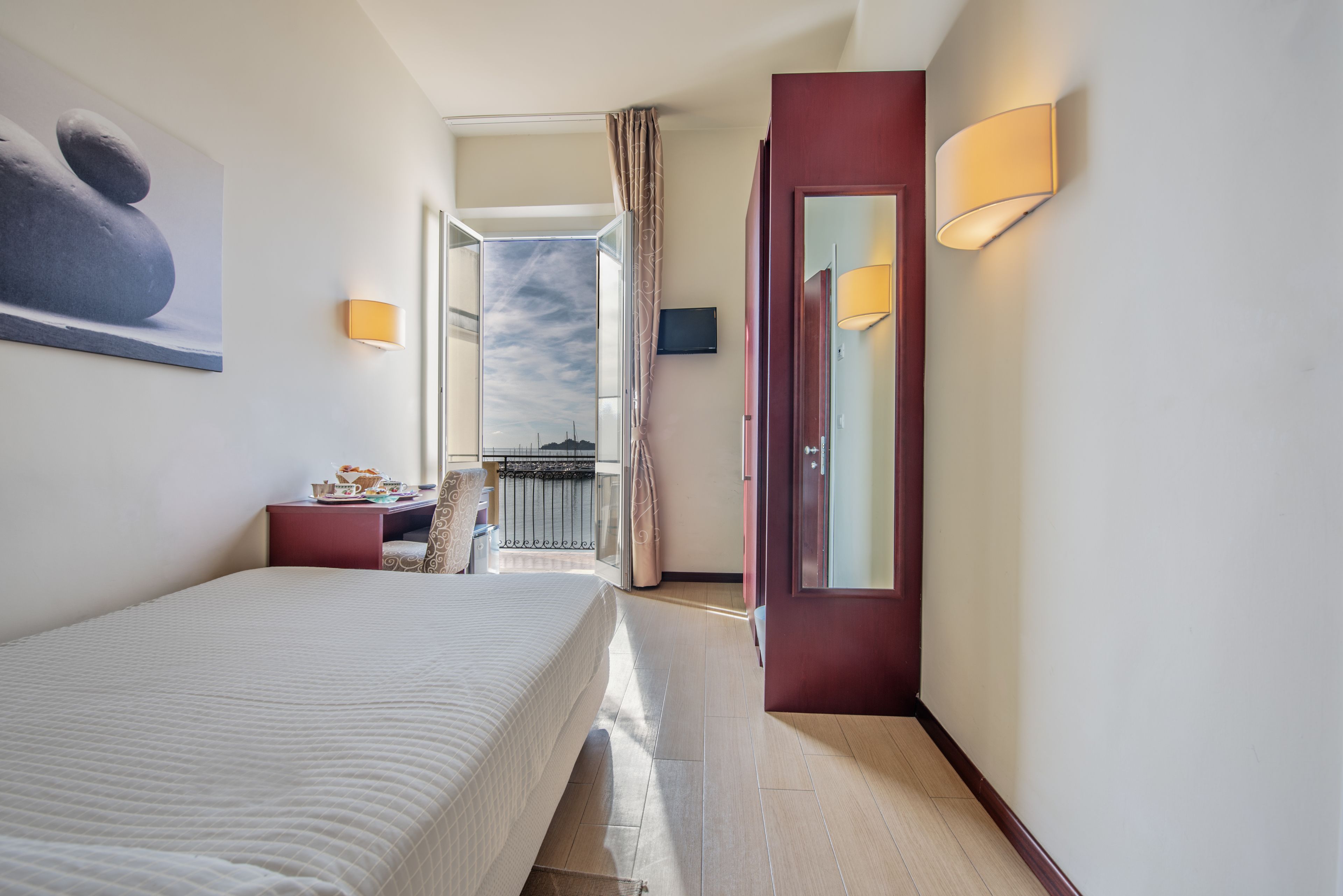 A hotel room with a bed, bedside table, lamp, and a view of the sky through a window.