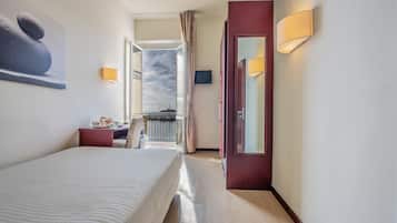 A hotel room with a bed, bedside table, lamp, and a view of the sky through a window.