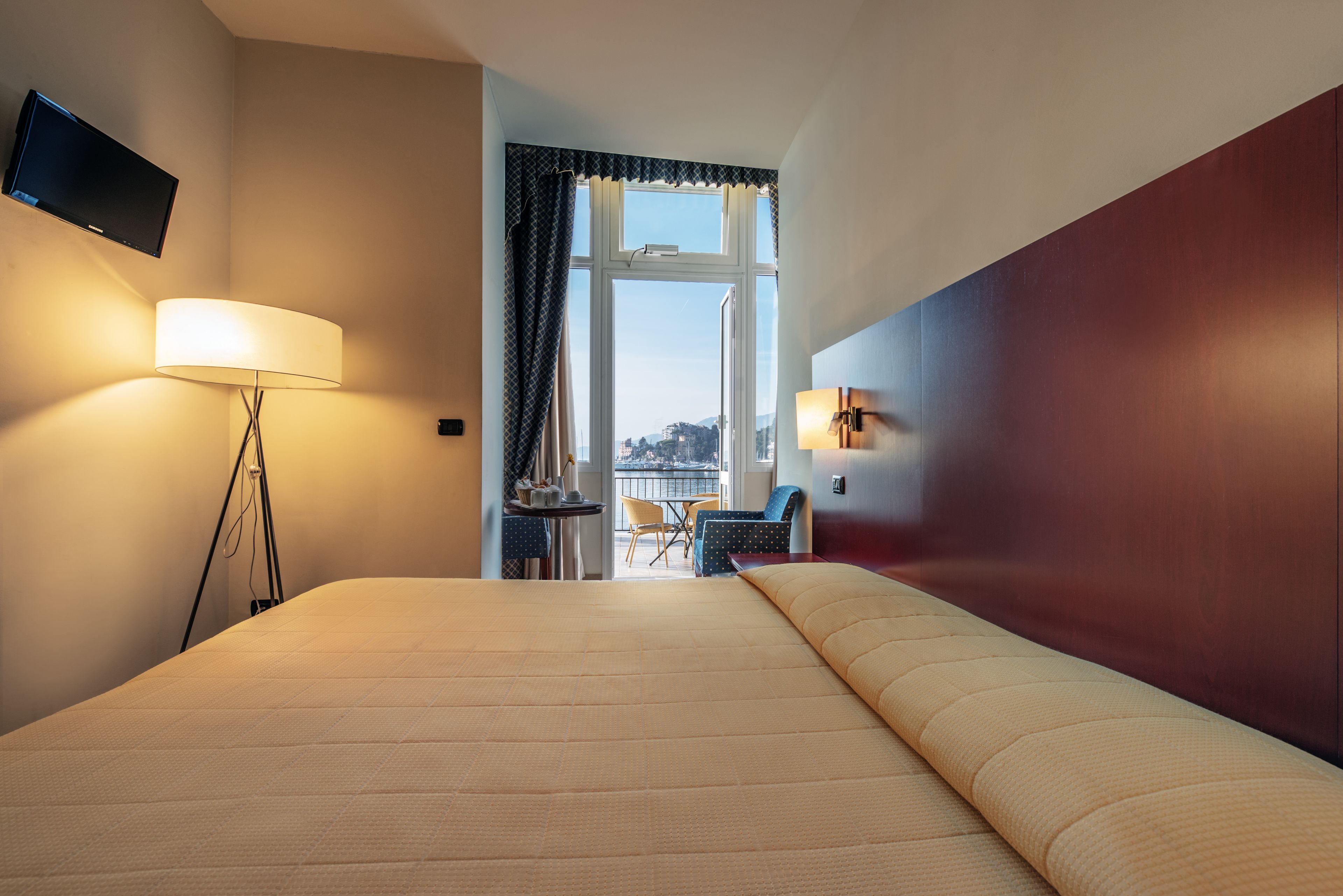 A hotel room with a large bed, a desk with a chair, a TV mounted on the wall, and a window with curtains.